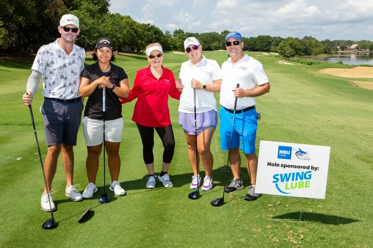 A foursome on the tee beside a hole-sponsor sign for Swing Lube