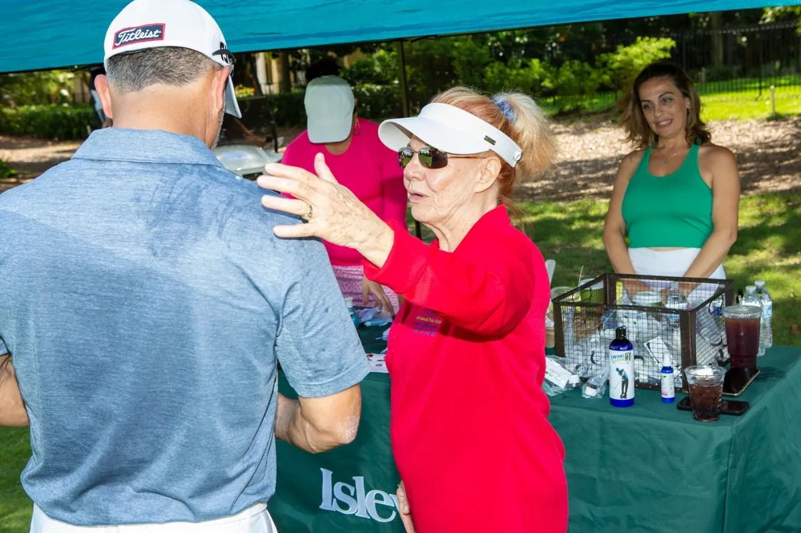 Phyllis at a golf tournament tent, applying Swing Lube to a player's shoulder herself.